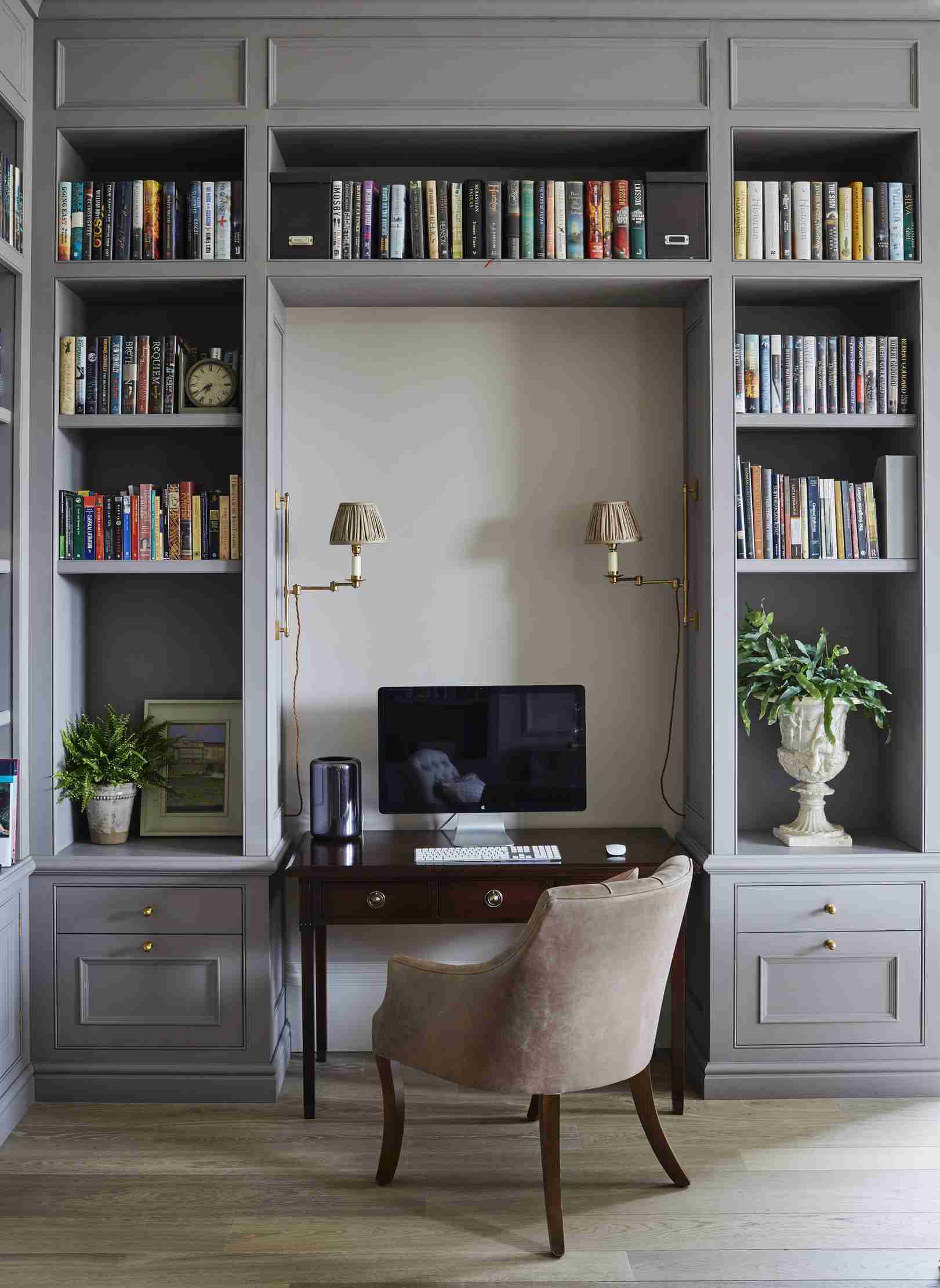 A desk set into a fitted bookcase niche with two wall-mounted lights directed toward the work area. Source interior example: Future.